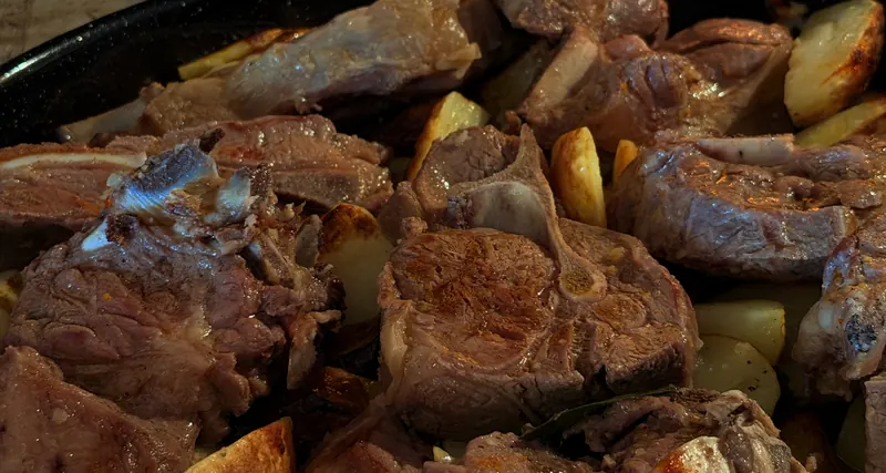 Meso ispod peke s krumpirom u teći, žeravica u pozadini